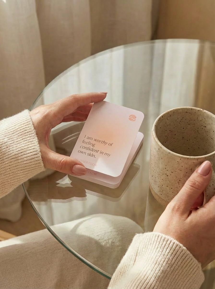 Person holding a stack of affirmation cards next to a mug on a glass table.
